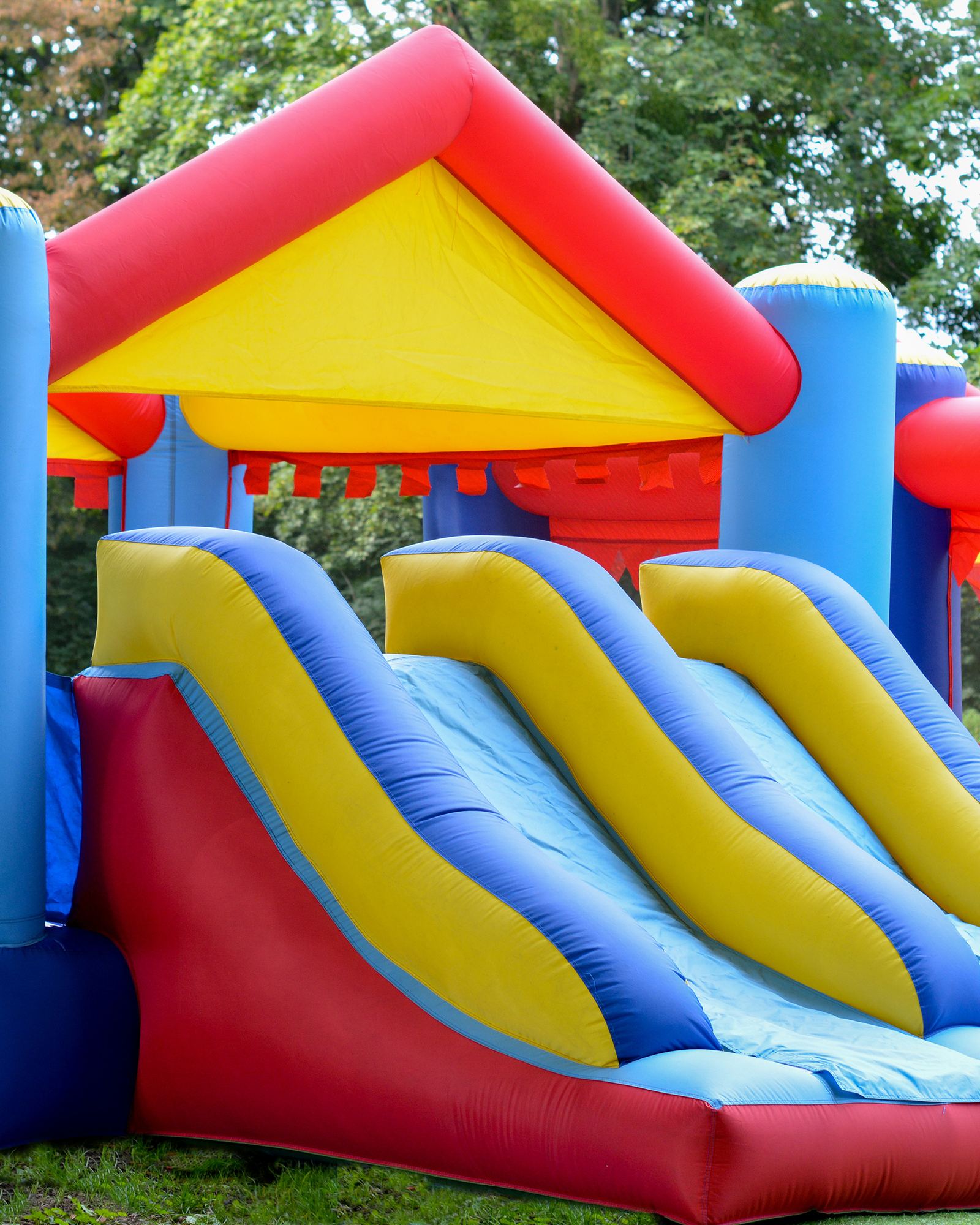 Red, yellow and blue bounce house combo with a triple slide, set up on a park lawn