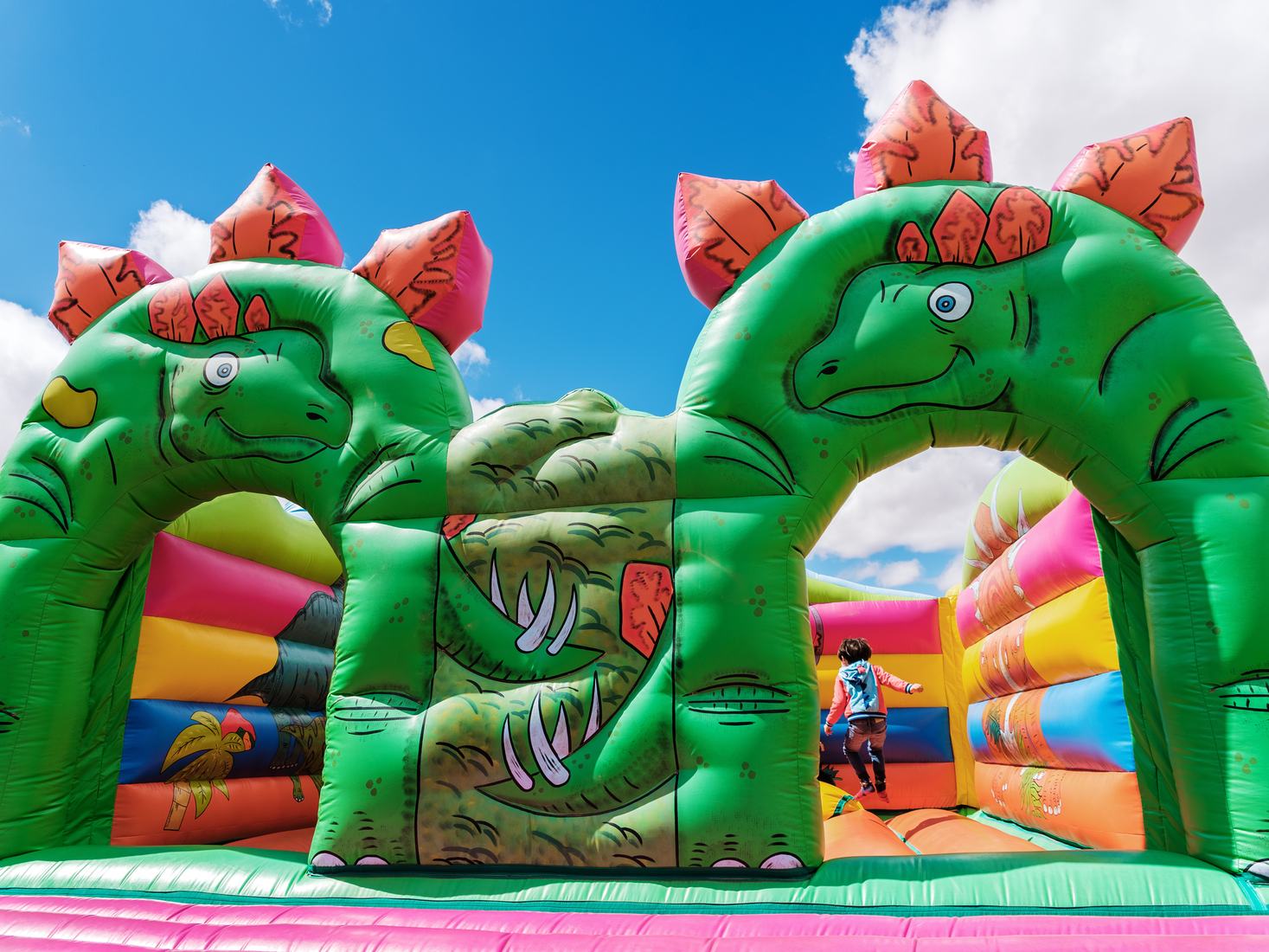 Green dinosaur bounce house with two arches and a child jumping inside