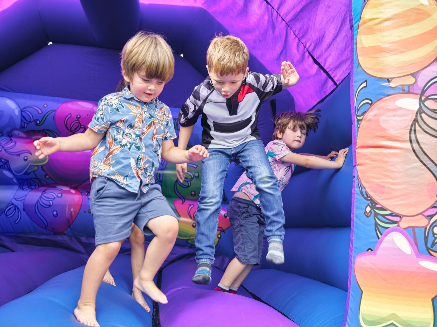 Three kids jumping together in a purple bounce house