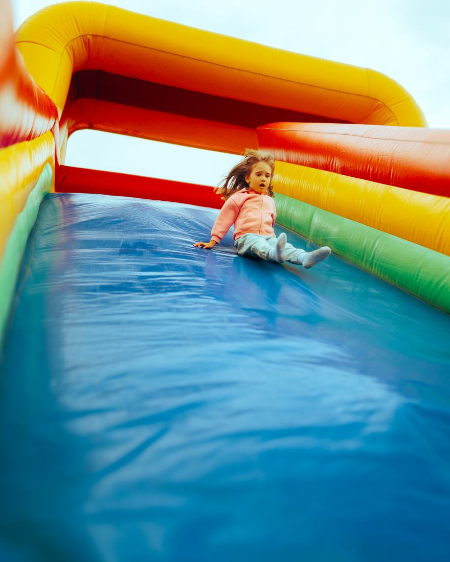 Girl sliding down a tall orange and blue inflatable slide