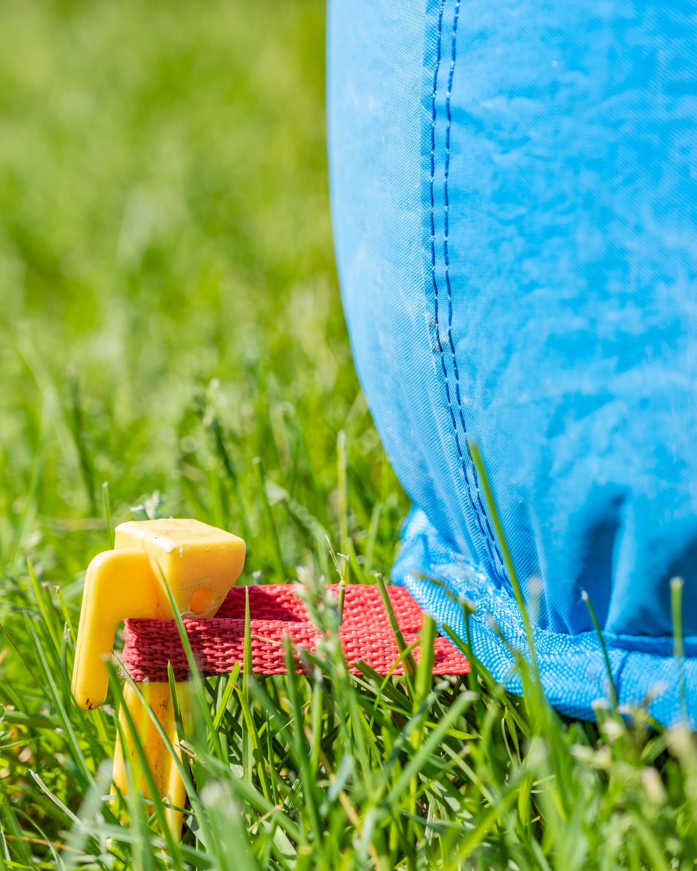 Yellow ground stake holding a red anchor strap on a blue bounce house, set in green grass